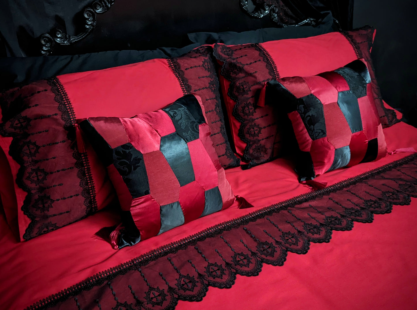 Red and black satin coffin patchwork cushions on a bed with black lace on red duvet cover and pillowcases with an ornate black headboard.