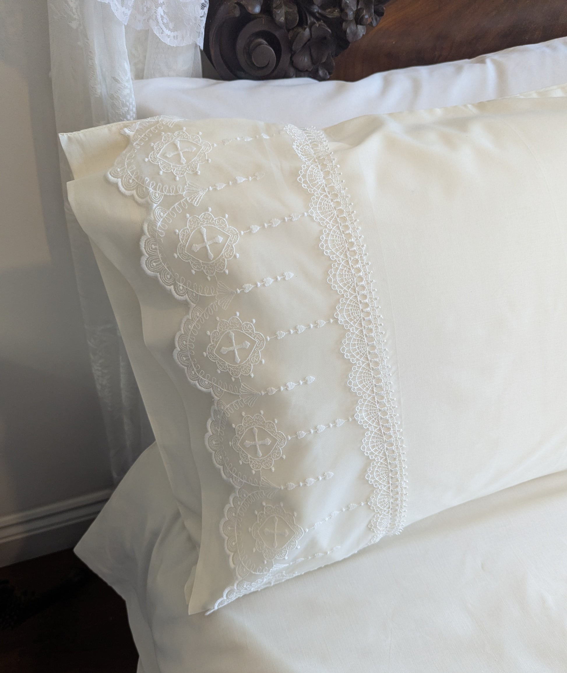Close-up of a cream pillow with white lace trim on a bed.