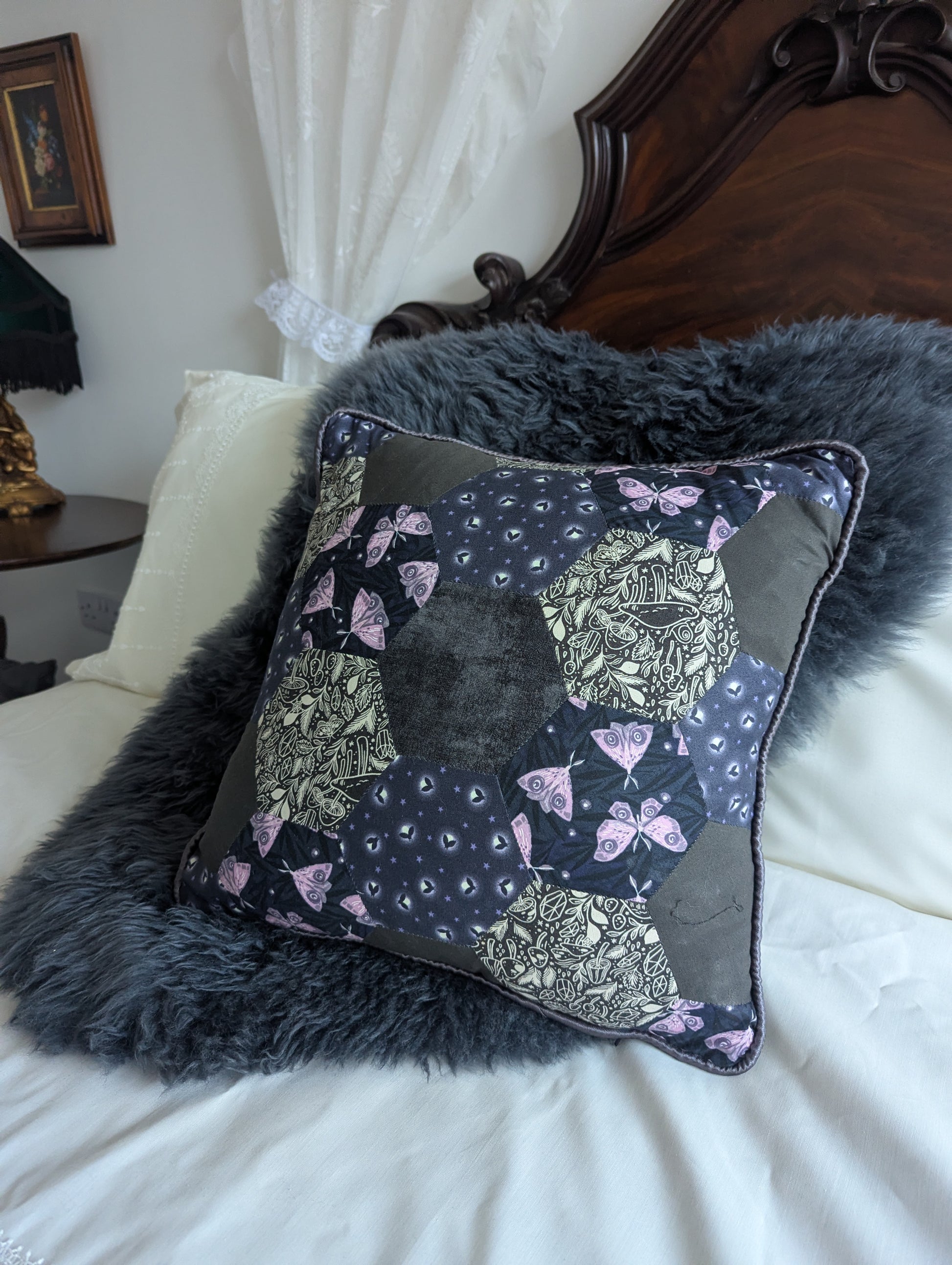 Decorative pillow with moths and fireflies on a bed with a fur throw