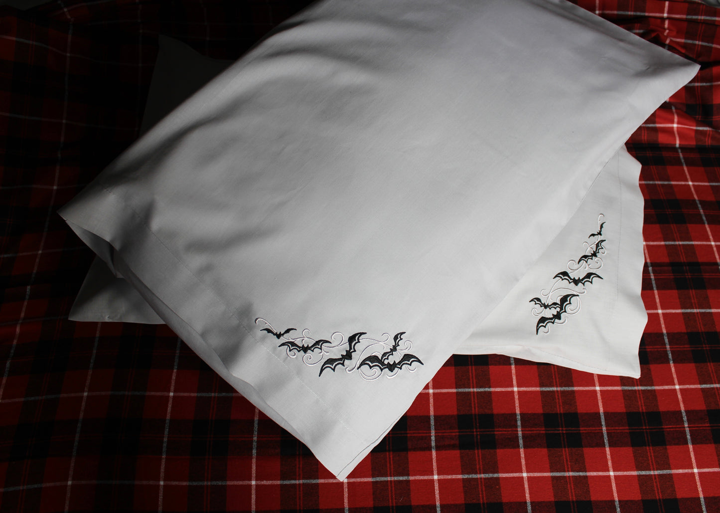 Black bats and grey scrolls embroidered on silver grey pillowcases on an orange tartan background 